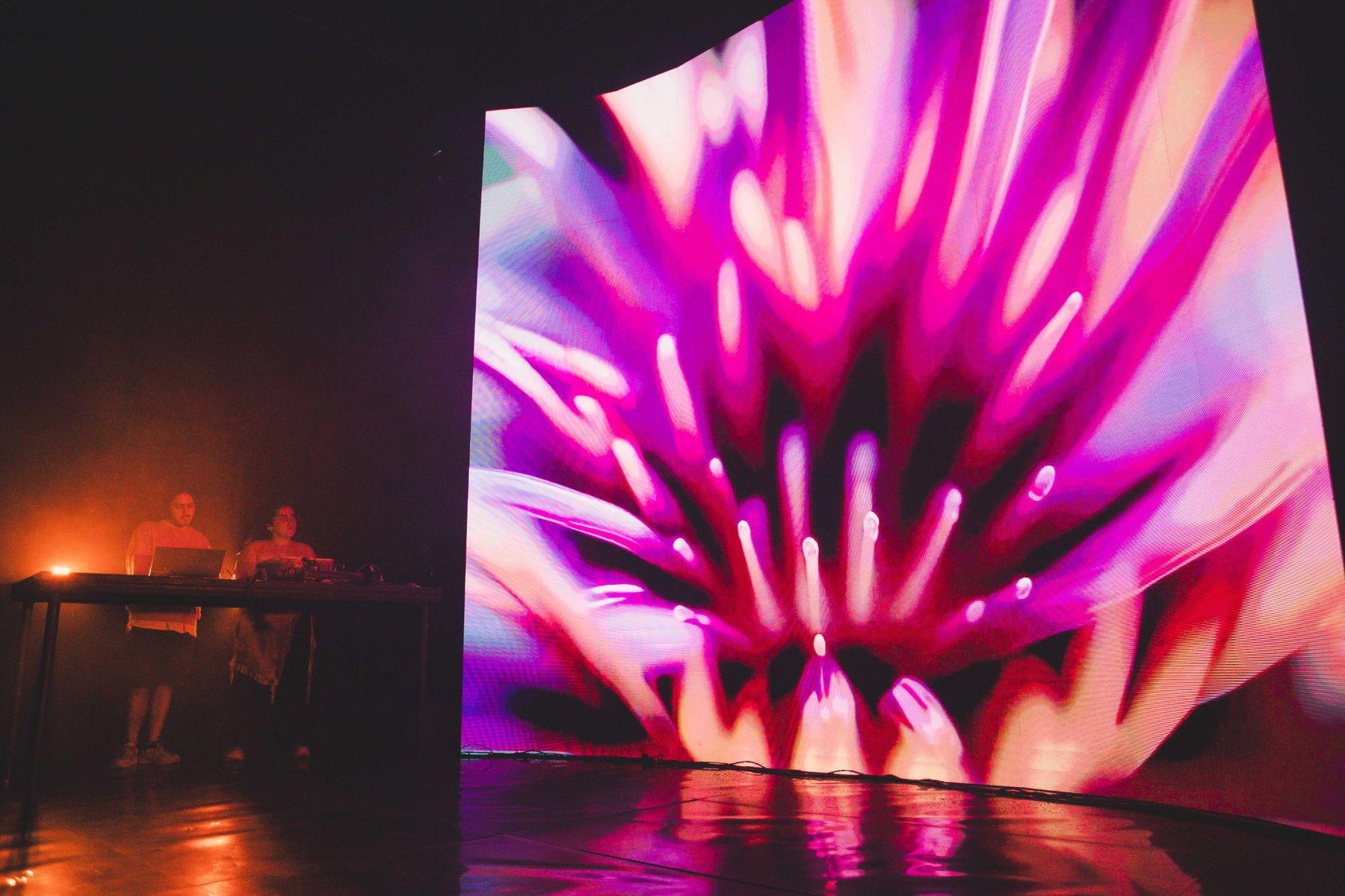 Performance stage with red light and large magenta projection.