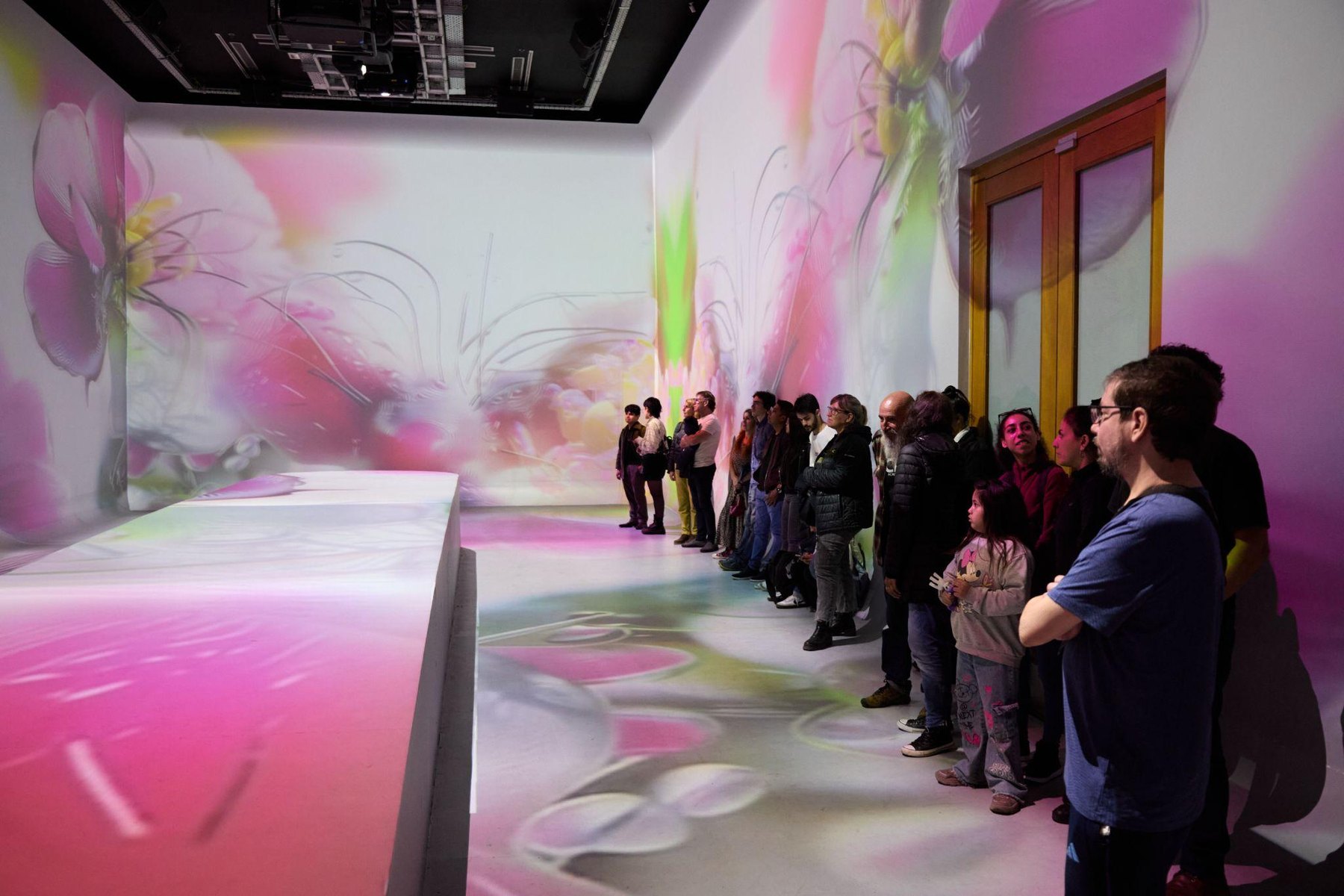 Audience seated in a gallery with pink projection.