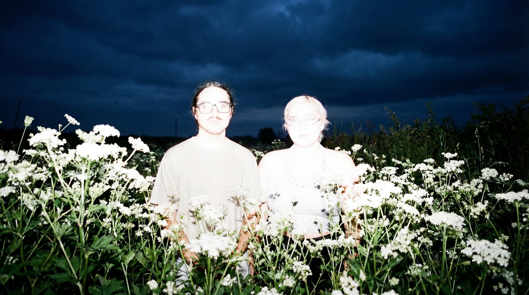 María Constanza Lobos and Sebastián Rojas photographed in a field of white flowers under a dark sky.